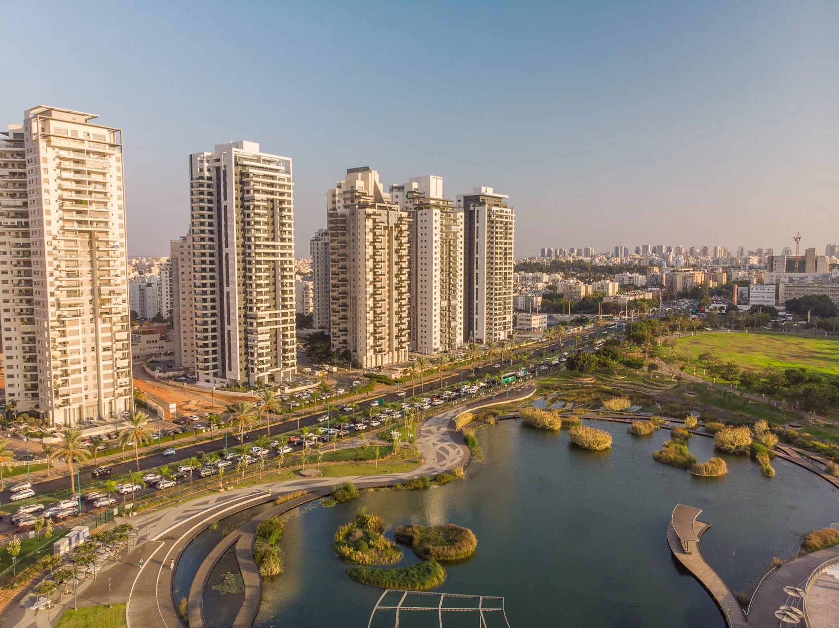מבט מהאוויר על מגדלי מגורים לצד כביש, פארק ואגם בפתח תקווה