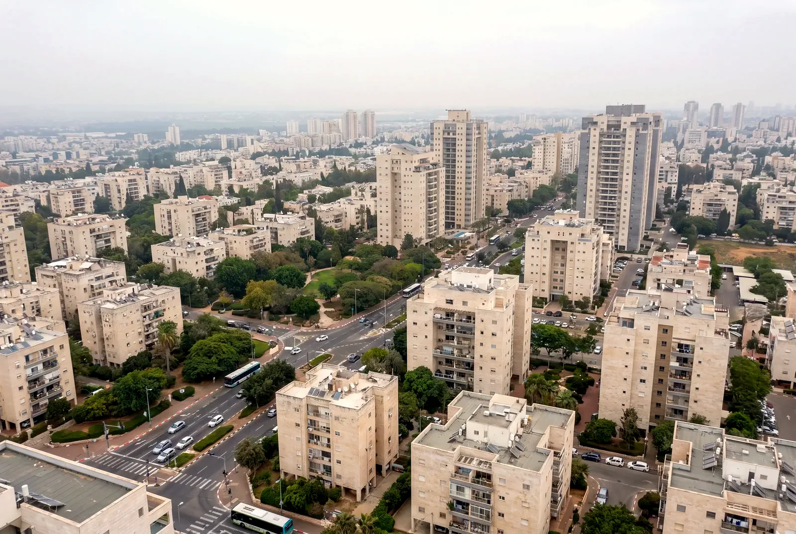 הדמיה: מבט רחב מגובה על עיר עם בנייני מגורים, מגדלים וצמרות עצים בערפל קל.