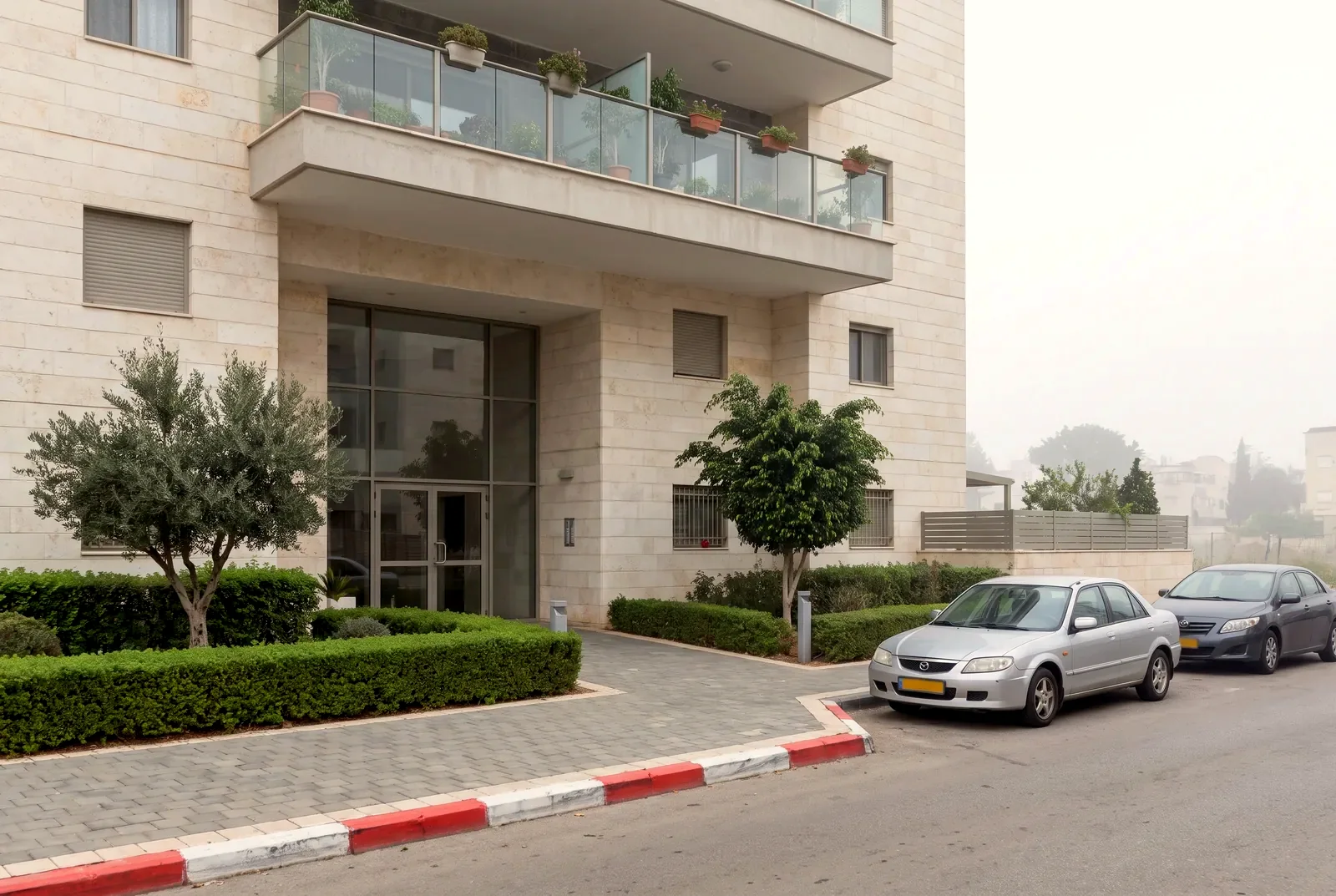הדמיה: כניסה לבניין מגורים חדש מצופה אבן, עם גינה מסודרת ומרפסות זכוכית