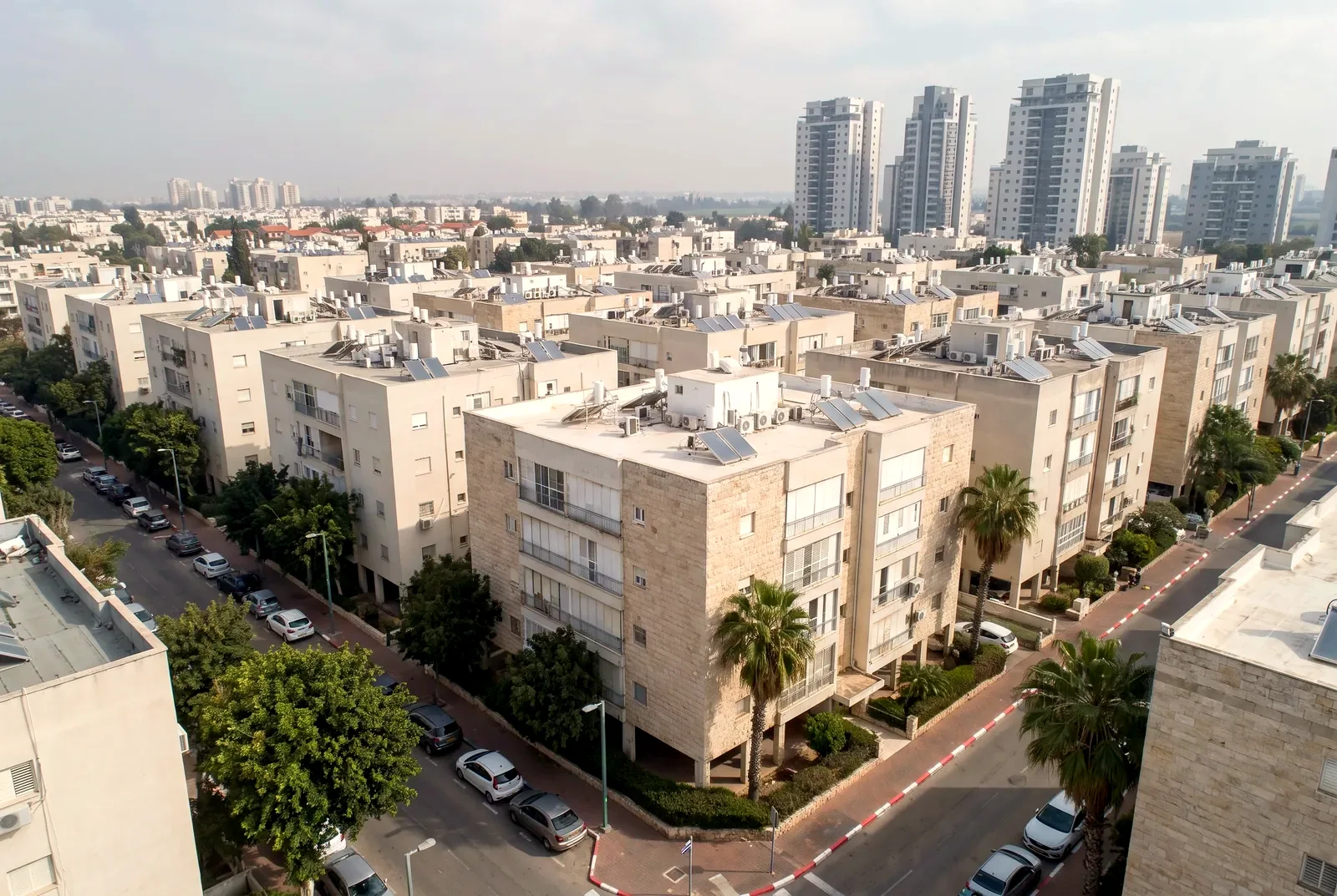 Illustration: an angled aerial view of a residential neighborhood with well-kept apartment buildings, trees and a few towers on the horizon