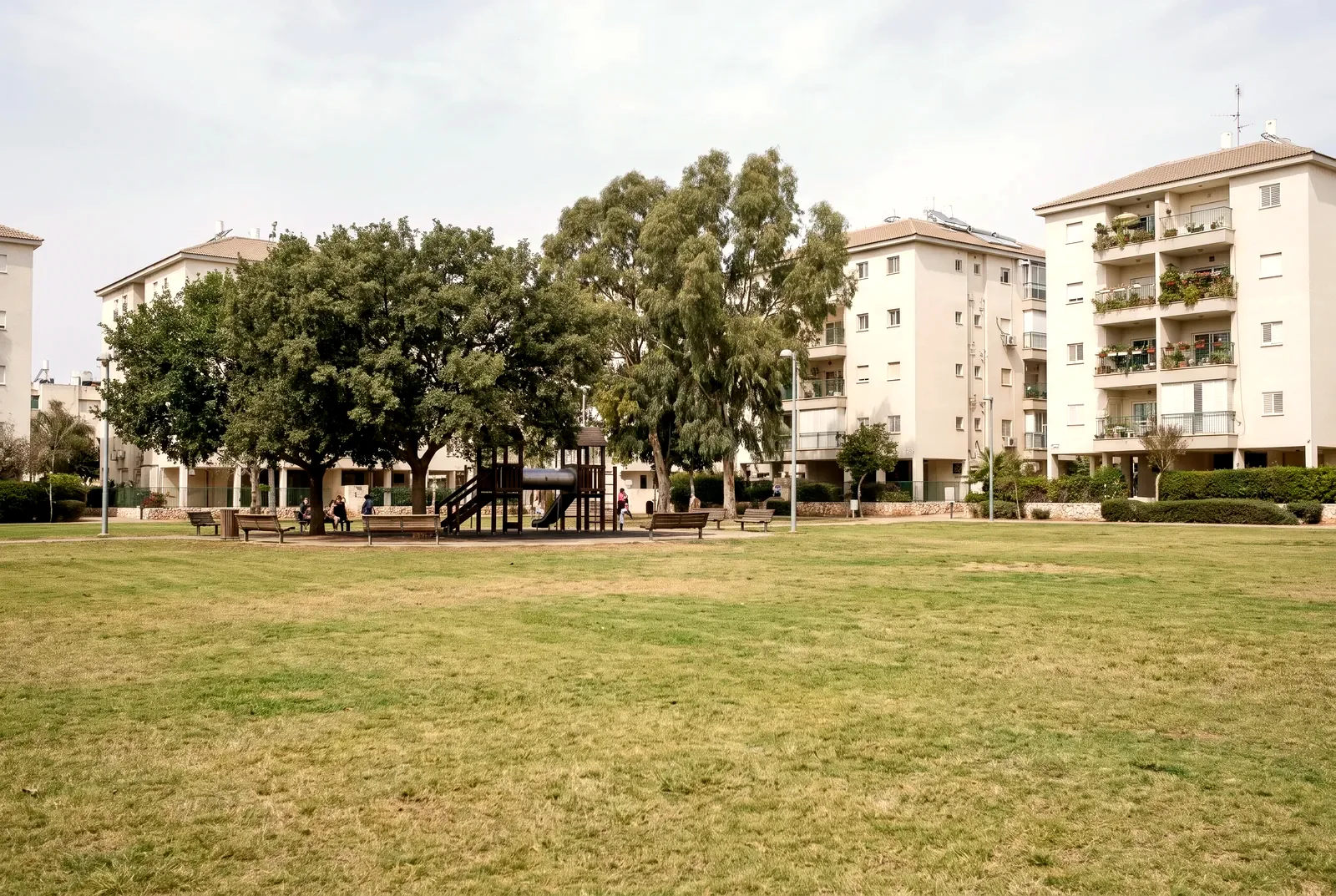 הדמיה: פארק שכונתי עם מגרש משחקים, ספסלים ועצי צל ובנייני דירות ברקע