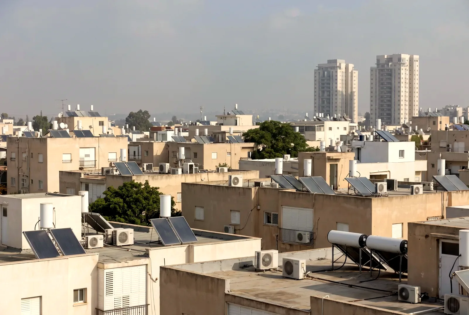 הדמיה: מבט מגג על גגות שטוחים של בנייני דירות עם דודי שמש ומגדלי מגורים באופק