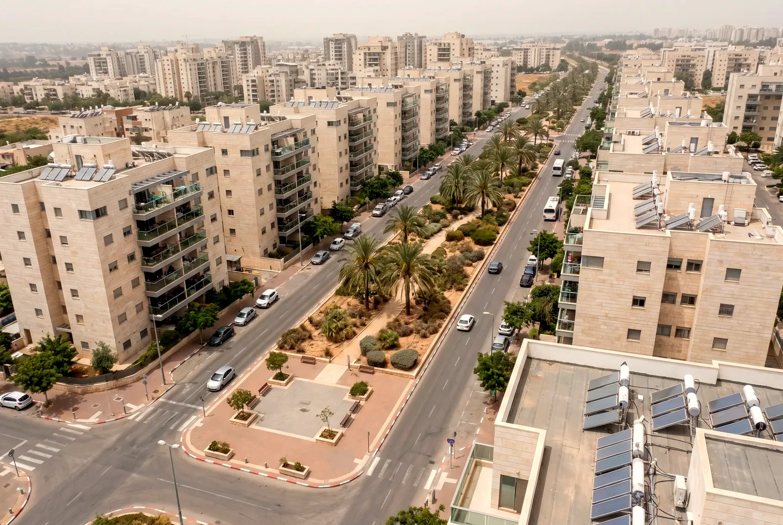 הדמיה: מבט אלכסוני מלמעלה על שכונה חדשה עם בנייני מגורים מצופי אבן ושדרה רחבה עם דקלים