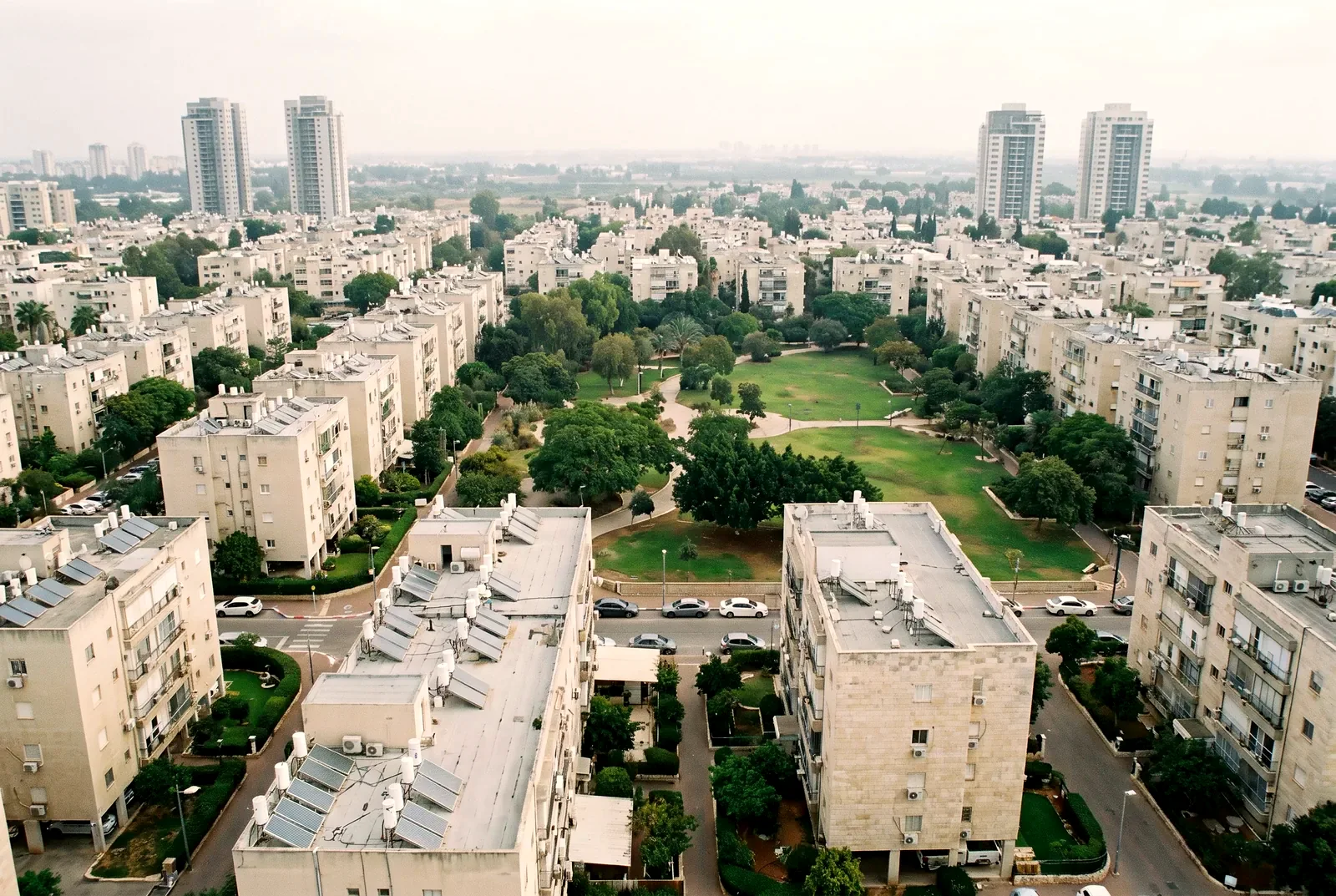 הדמיה: מבט אלכסוני מלמעלה על שכונת מגורים עם בנייני דירות, פארק ירוק במרכזה ומגדלי מגורים באופק