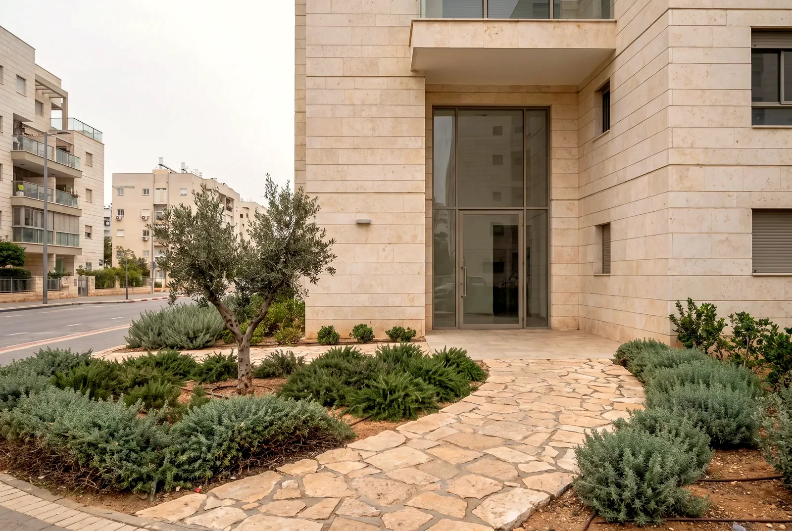 הדמיה: כניסה לבניין מגורים חדש עם גינה מטופחת בחזית