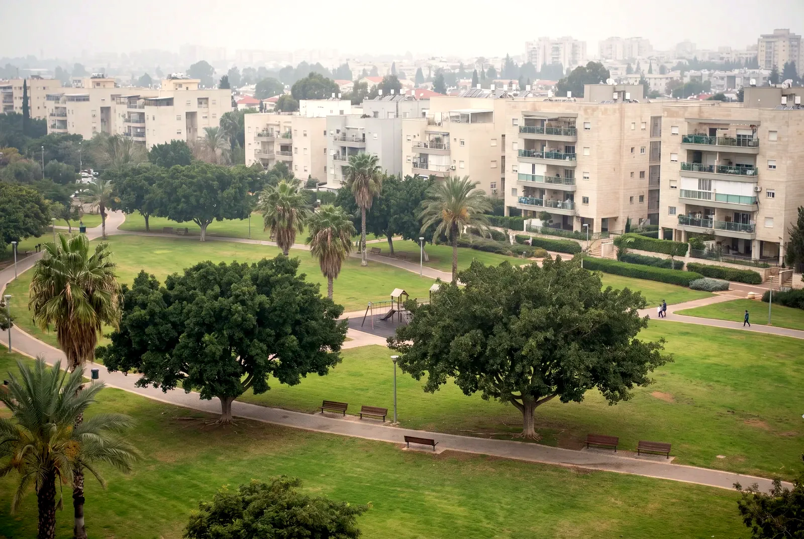 הדמיה: פארק שכונתי מרחוק עם דשא, עצים ובנייני מגורים ברקע