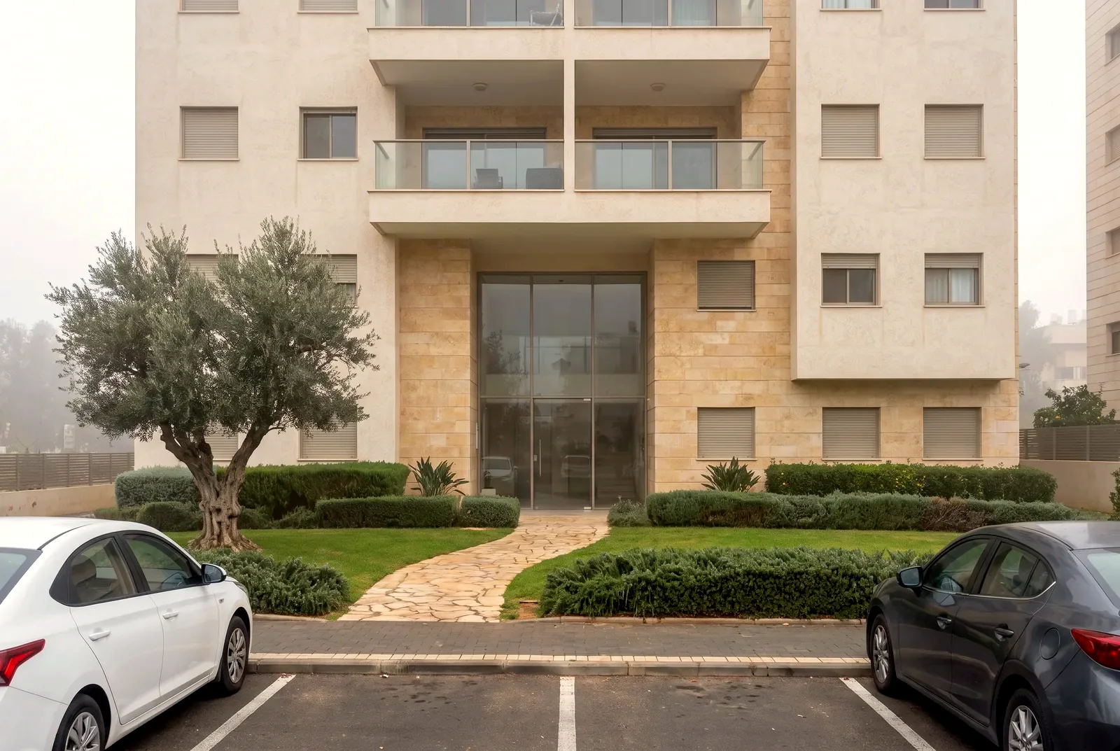 הדמיה: חזית וכניסה של בניין דירות מודרני בן שש קומות עם גינה מסודרת ושביל אבן