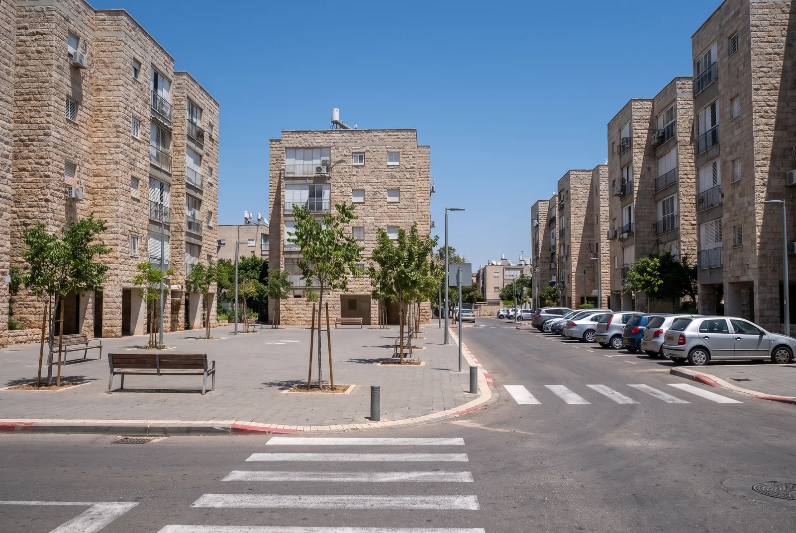 הדמיה: פינת רחוב מטופחת עם בנייני מגורים ורחבה קטנה עם ספסלים