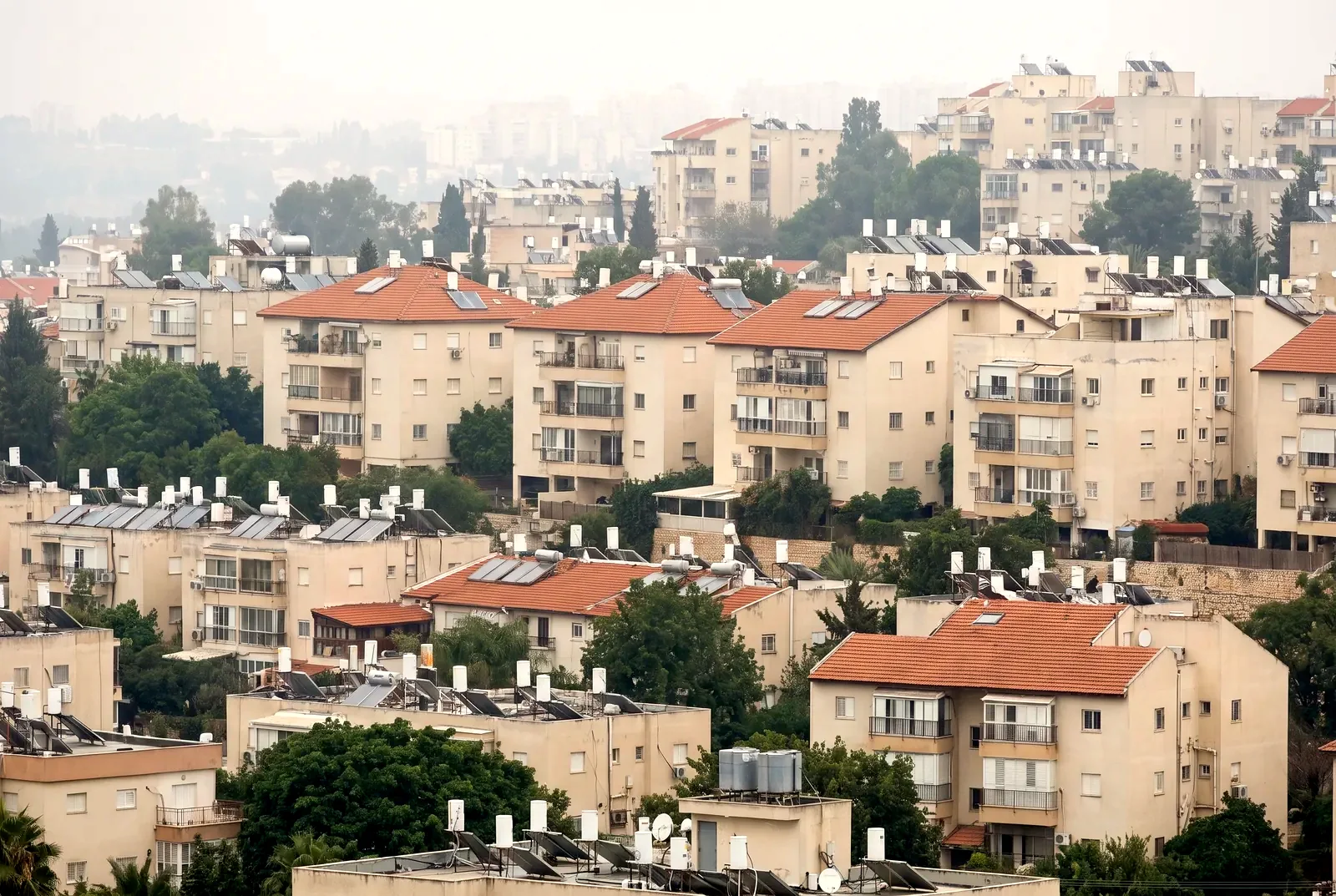 הדמיה: מבט טלסקופי דחוס על שכבות של בנייני מגורים וגגות שטוחים בערפל קל.