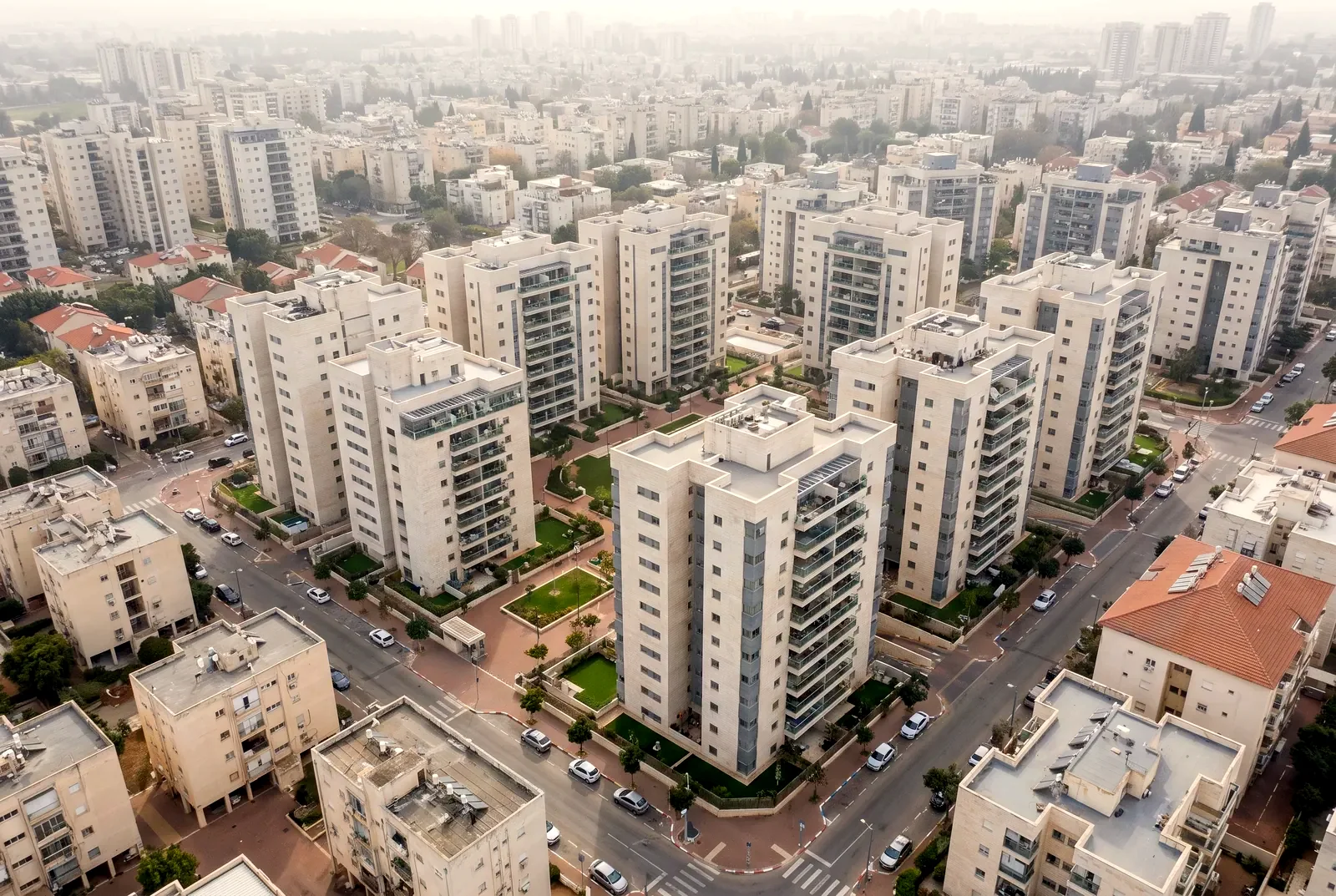 הדמיה: מבט מרחפן באלכסון על אזור חדש בעיר עם בנייני דירות מחופי אבן וחצרות מגוננות.