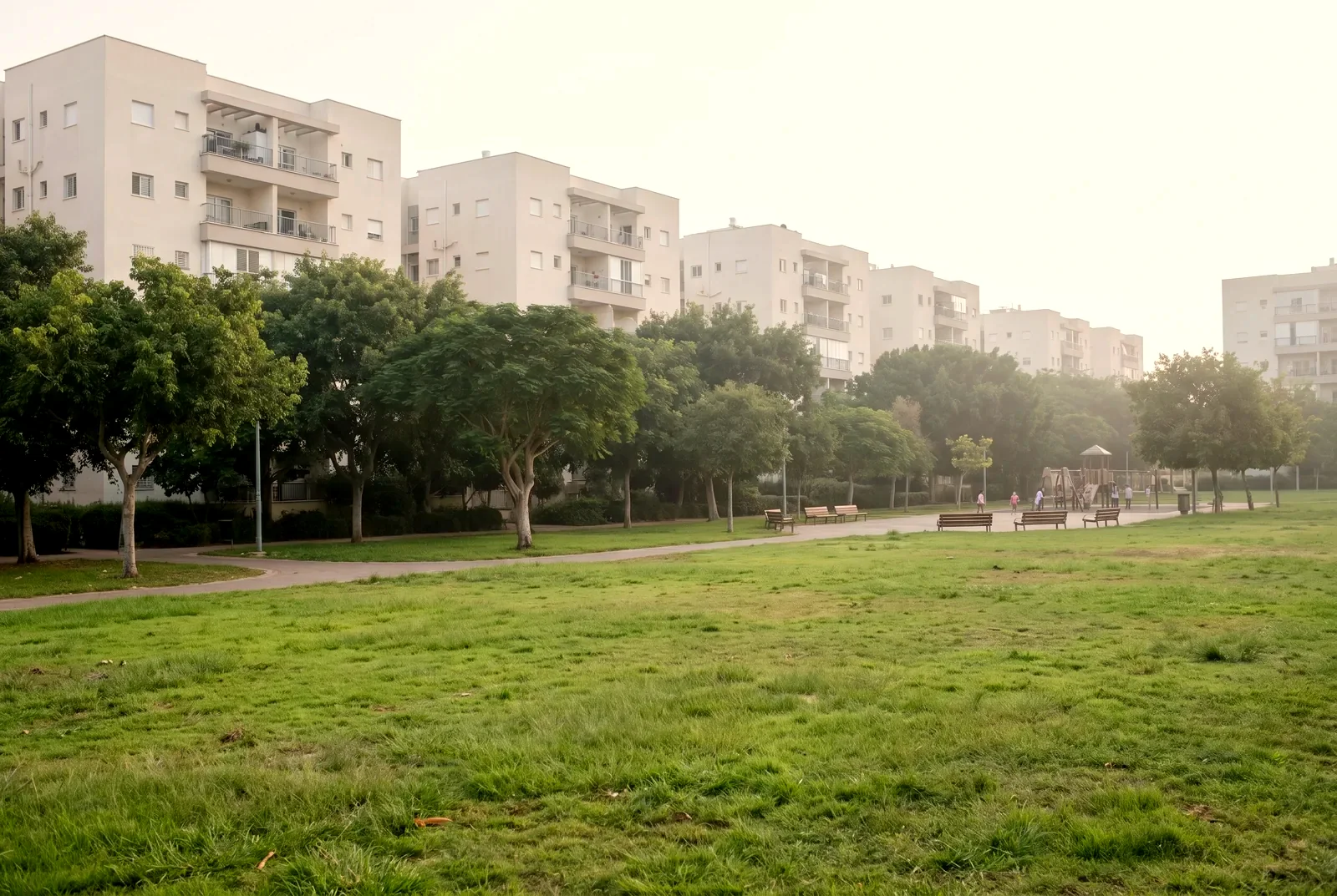 הדמיה: פארק שכונתי במבט מרחוק, עם שבילים ובנייני דירות מאחורי העצים.