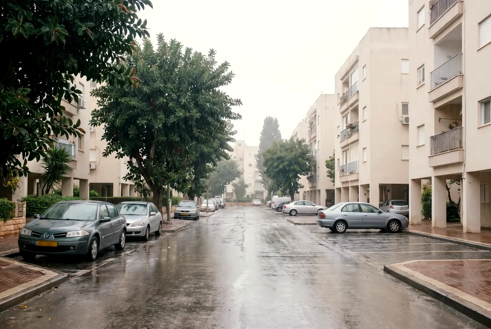 הדמיה: רחוב שקט בשכונת מגורים מיד אחרי גשם, עם אספלט רטוב, עצי פיקוס ובנייני דירות מטופחים.