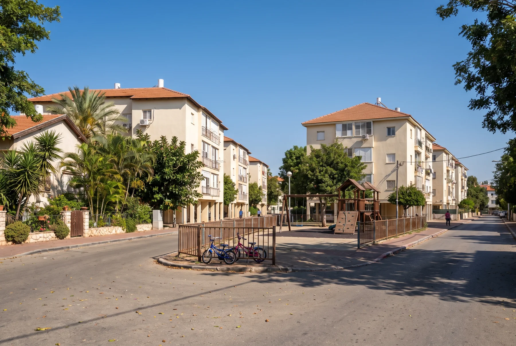 הדמיה: רחוב מגורים שקט עם בתים נמוכים, עצי דקל וגינת משחקים קטנה